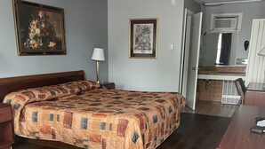 A hotel room with a large bed, a desk, a chair, a lamp, and a bathroom visible through an open door. - Budget Host Three Crowns Motor Lodge (Gettysburg)