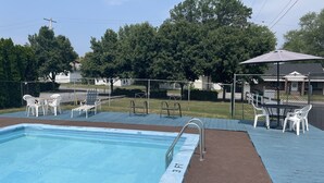 A swimming pool with a metal ladder, surrounded by a fenced deck with white plastic chairs and tables. - Budget Host Three Crowns Motor Lodge (Gettysburg)