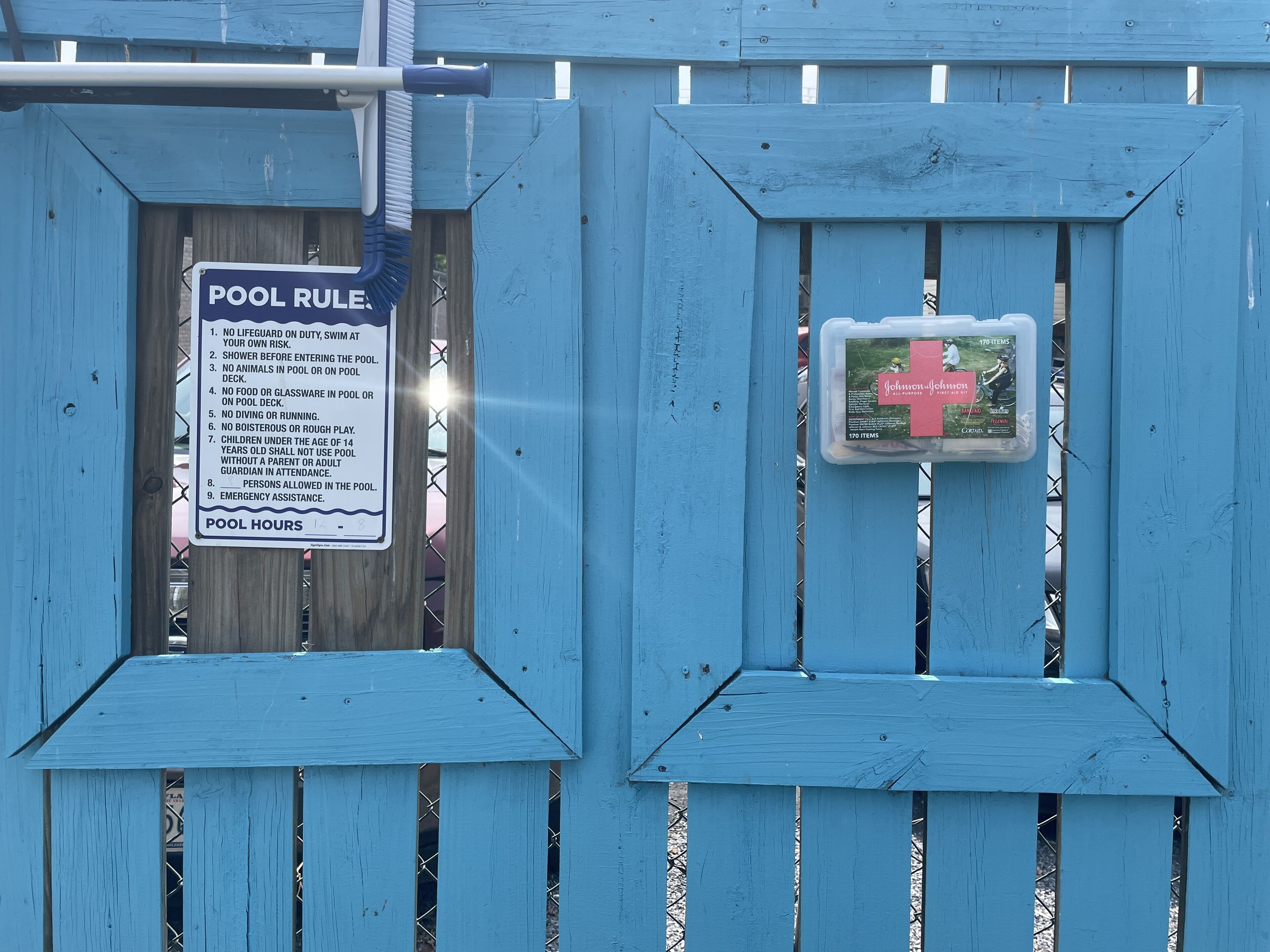 Una reja de madera azul para piscina, con un cartel de normas de la piscina y un botiquín.