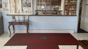 A reception area with a counter, framed documents, a small table, and a red carpet. - Budget Host Three Crowns Motor Lodge (Gettysburg)