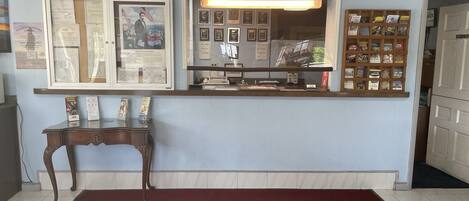 A reception area with a counter, framed documents, a small table, and a red carpet.