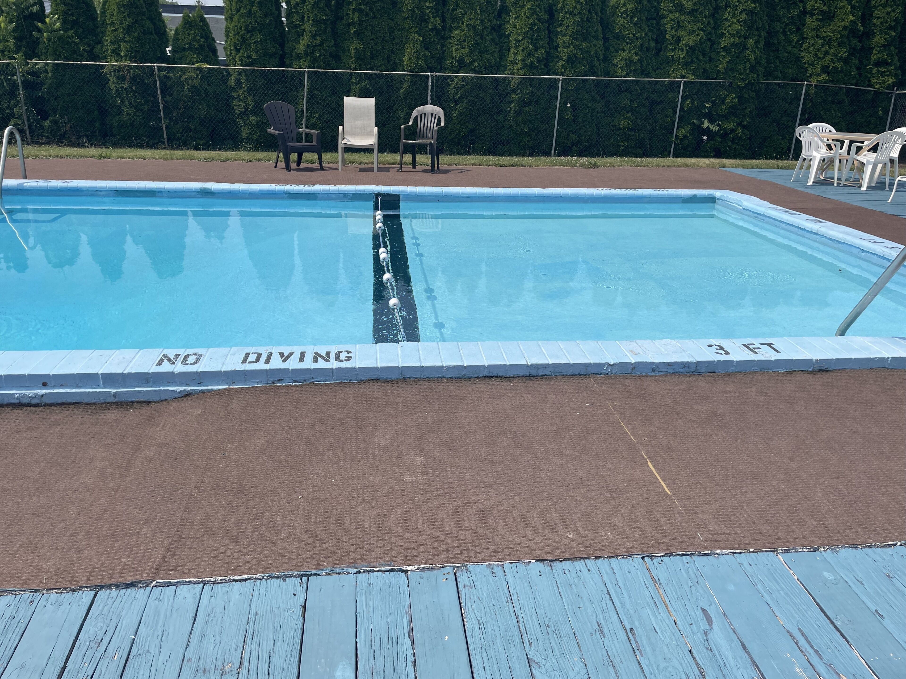 A rectangular swimming pool with a 'NO DIVING' sign, surrounded by a fence and chairs.