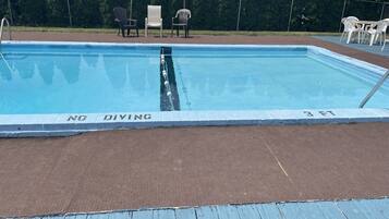 A rectangular swimming pool with a 'NO DIVING' sign, surrounded by a fence and chairs.