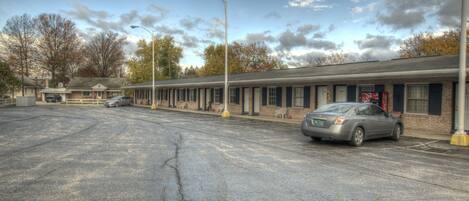 Un motel con aparcamiento, un edificio de una planta y una hilera de habitaciones con fachada de ladrillo.