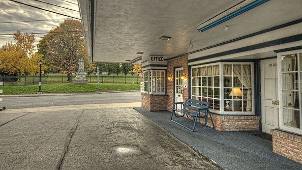 A gas station with a small office, a bench, and a statue in the background. - Budget Host Three Crowns Motor Lodge (Gettysburg)