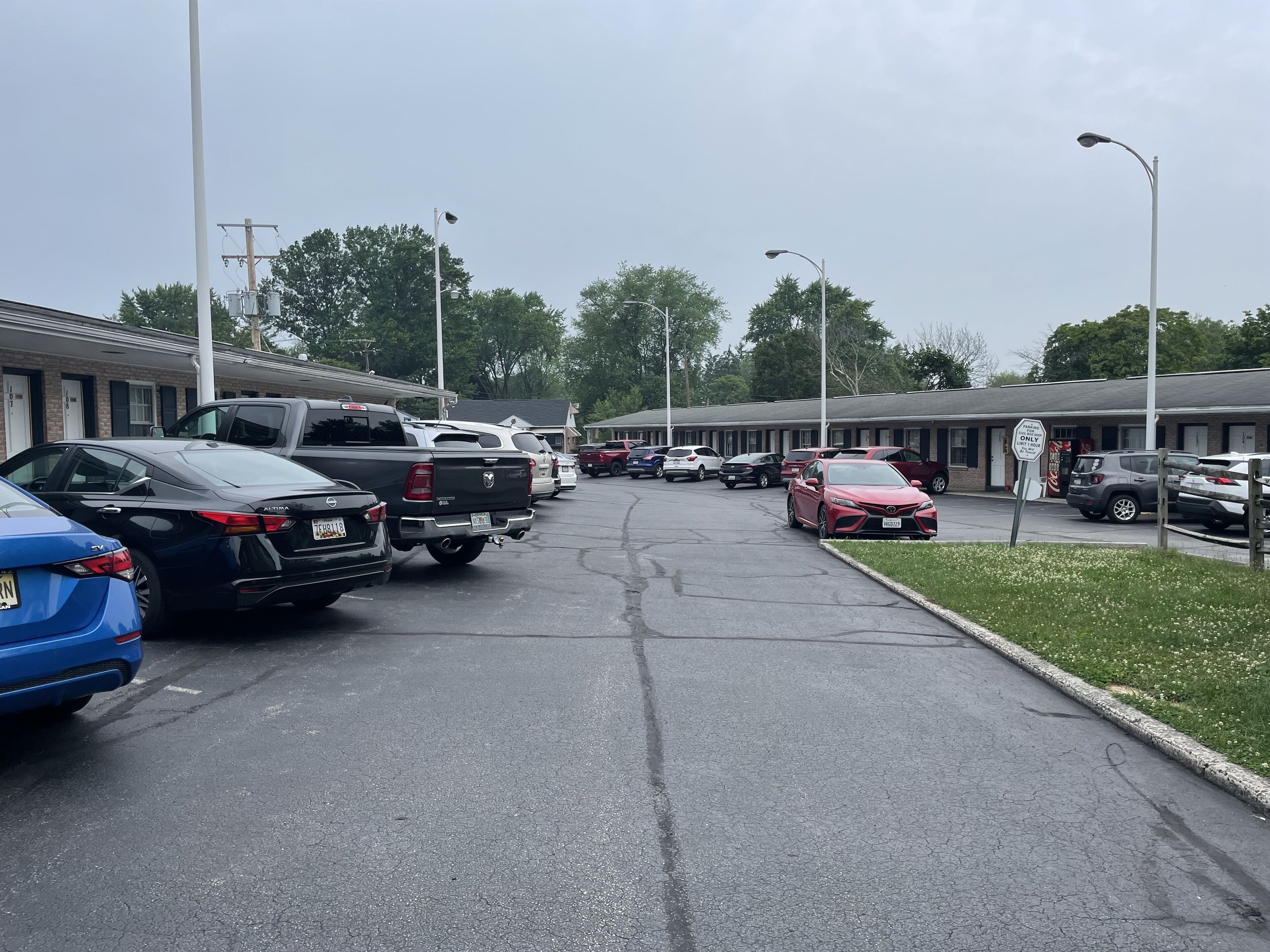 Un estacionamiento con varios vehículos, incluyendo coches y camiones, frente a un motel con múltiples habitaciones.