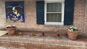 A brick wall with a large eagle mural, a window with dark shutters, and two terracotta pots with flowers. - Budget Host Three Crowns Motor Lodge (Gettysburg)