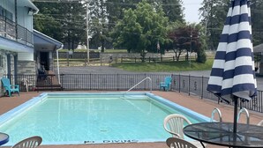 A swimming pool with a 'No Diving' sign, surrounded by chairs and tables, with a view of a park and a building in the background. - Colton Motel Gettysburg (Gettysburg)