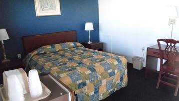 A hotel room with a bed, a desk, a chair, a lamp, and a picture on the wall.