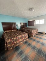 Habitación de hotel con dos camas, una mesita de noche, una lámpara y un ventanal con cortinas.