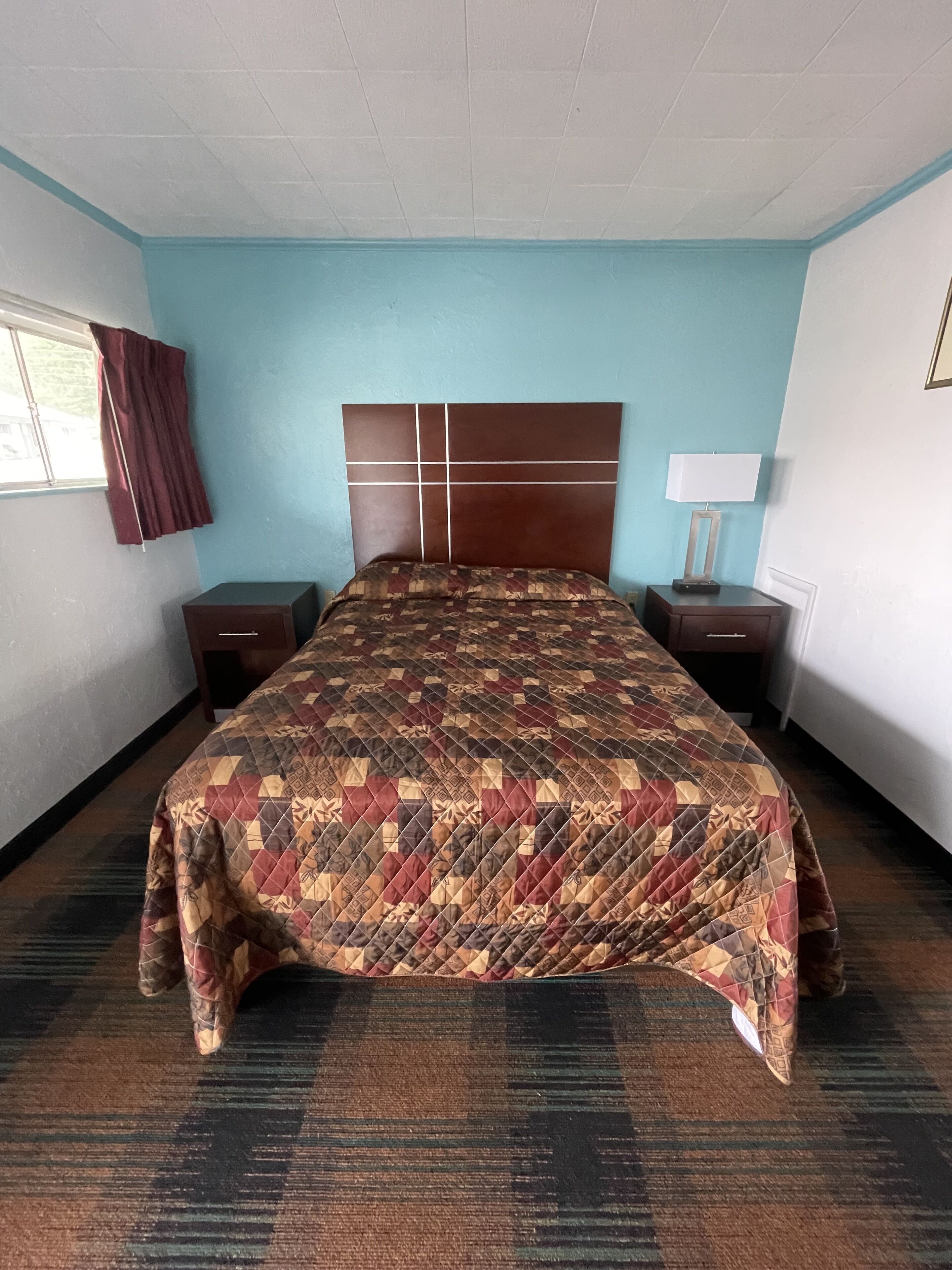 A hotel room with a large bed, a headboard with a grid design, two bedside tables, a lamp, and a window with curtains.