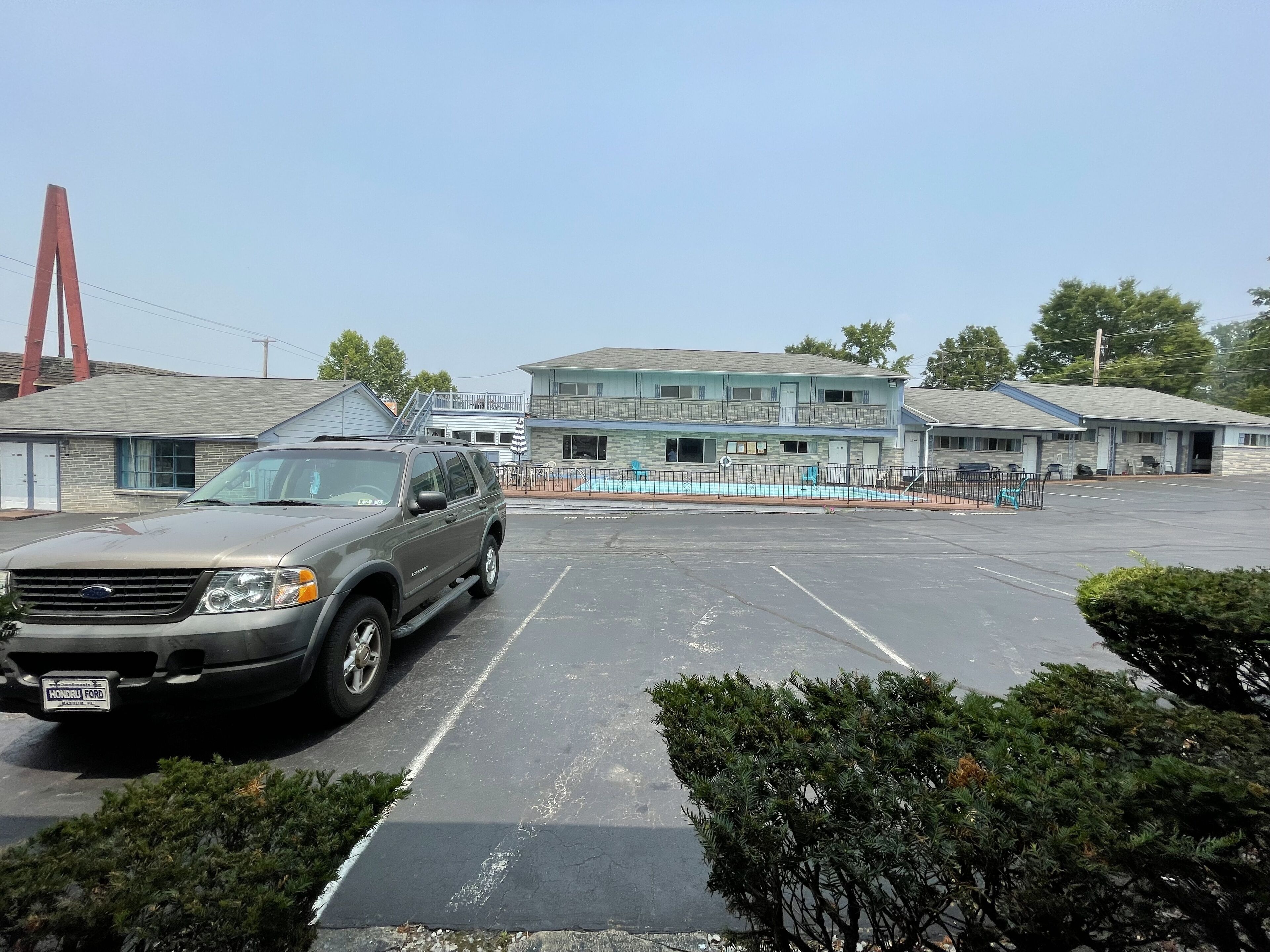 Un estacionamiento con un SUV Ford, un motel con piscina y un edificio con una grúa roja al fondo.