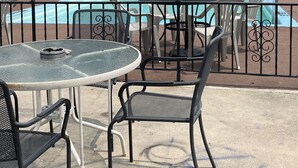 A poolside area with a glass table and chairs, a striped umbrella, and a view of a building with a balcony. - Colton Motel Gettysburg (Gettysburg)