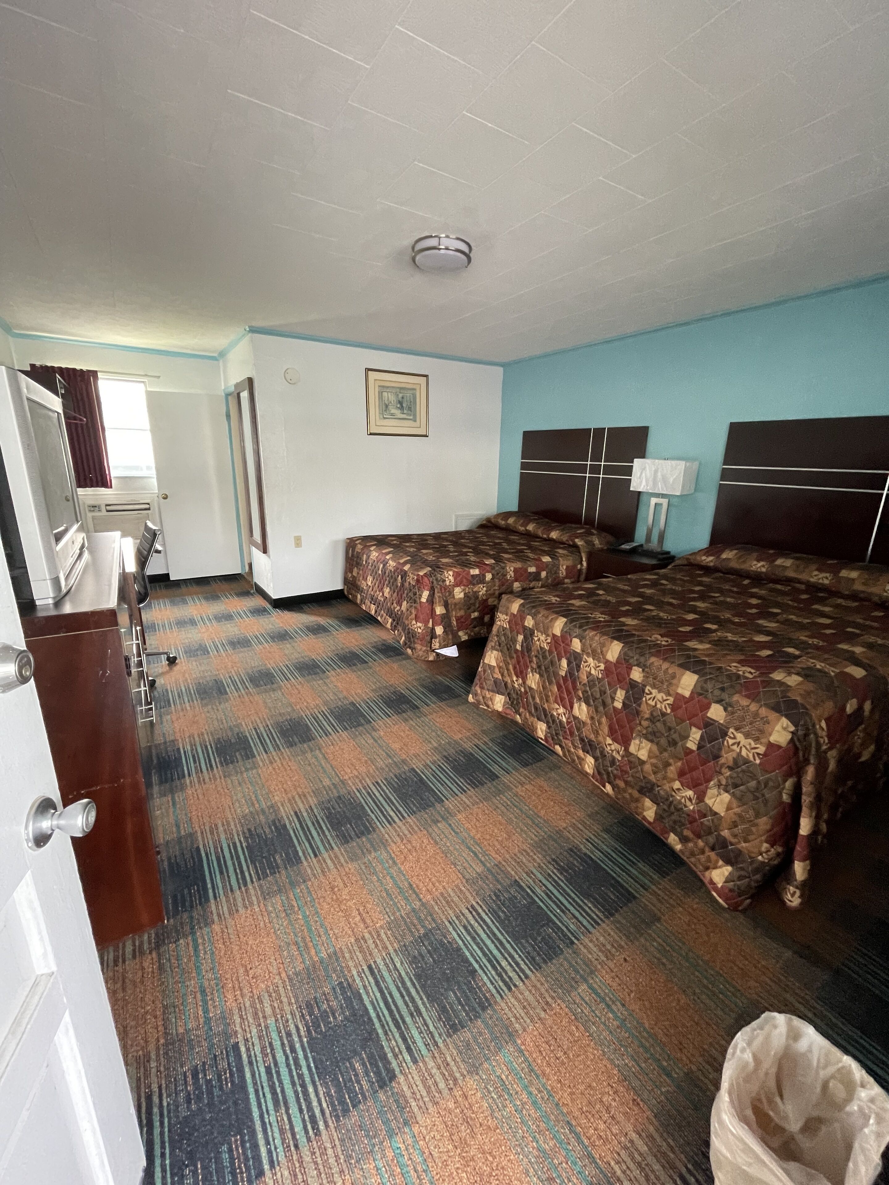 Une chambre d’hôtel avec deux lits, un bureau avec une chaise, une commode et une fenêtre avec des rideaux.