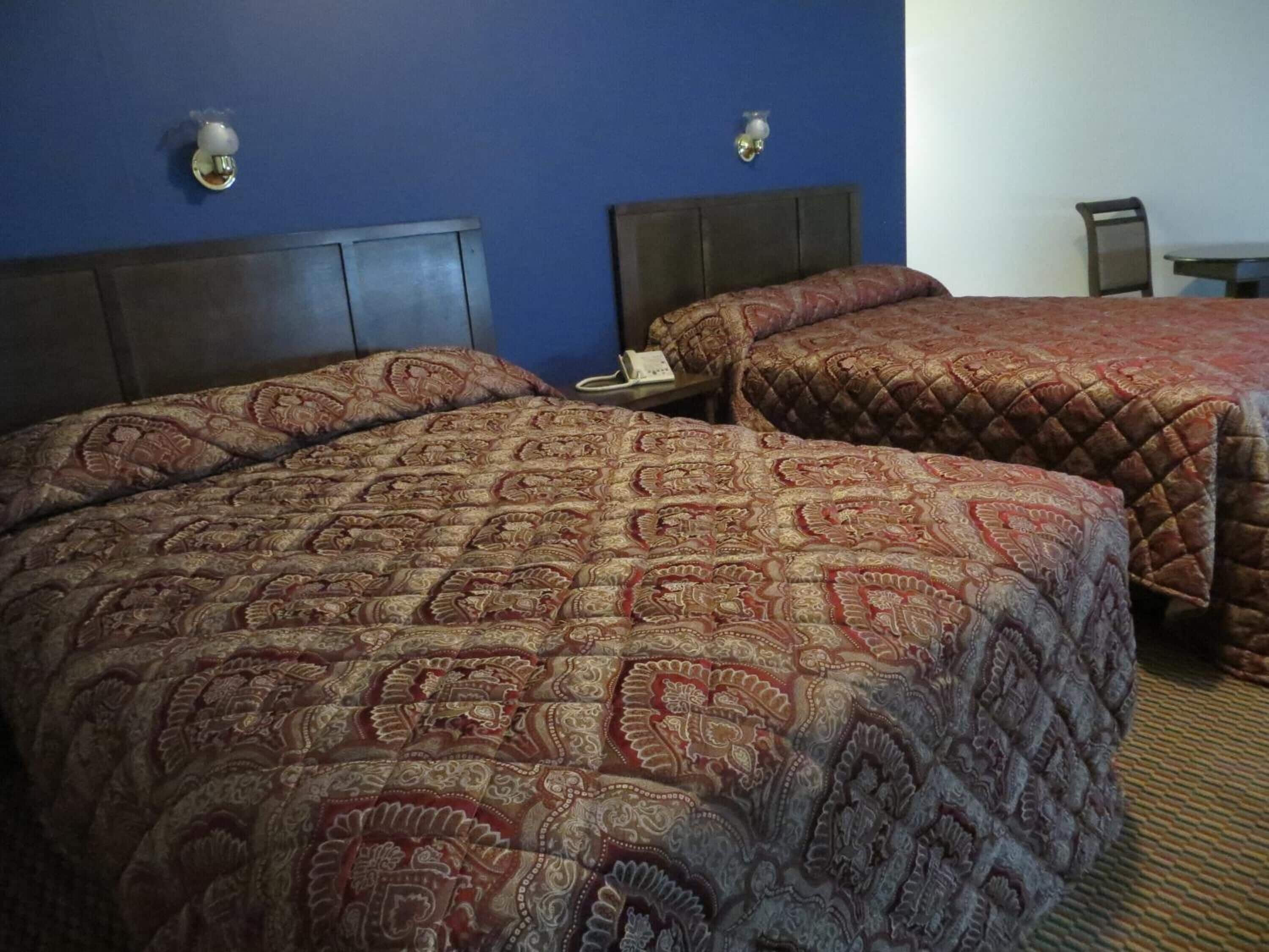 Two double beds with patterned bedspreads in a hotel room.