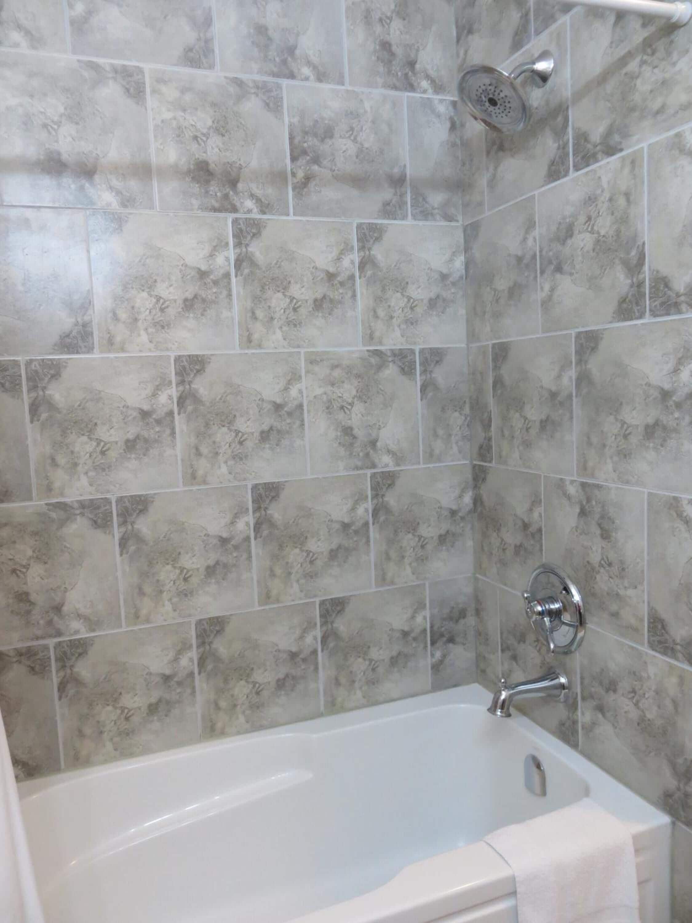 Baño con bañera, ducha y paredes de azulejos.