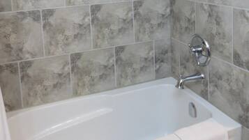 Baño con bañera, ducha y paredes de azulejos.
