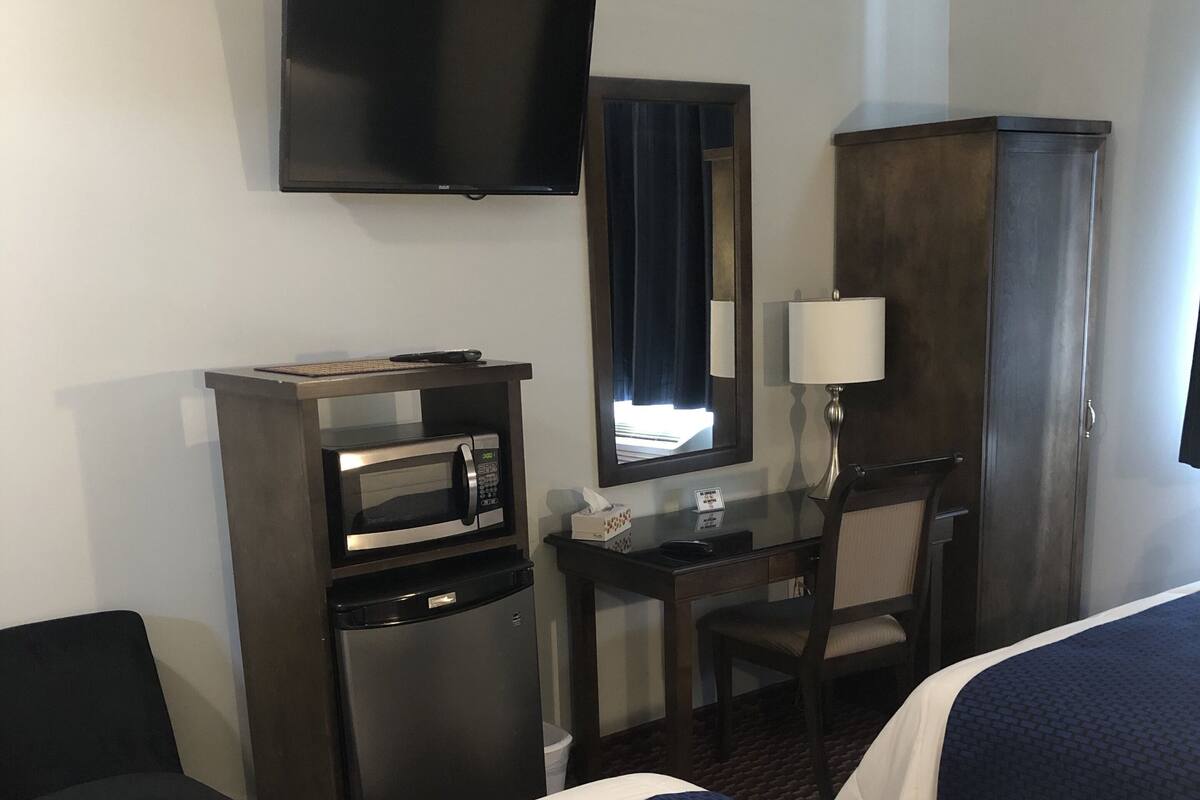 A hotel room with two beds, a desk with a computer, a television, a minibar, and a wardrobe.