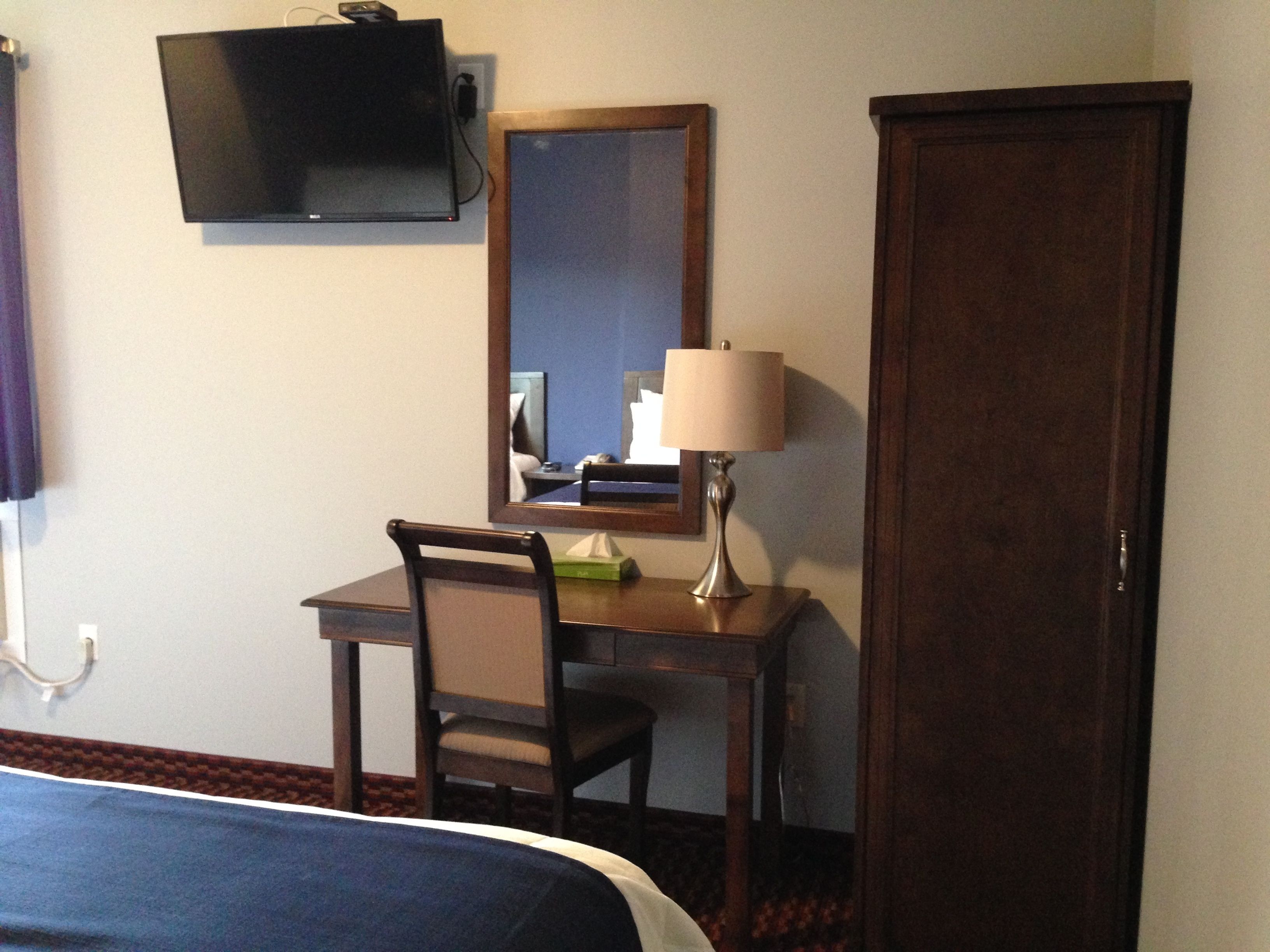 Habitación de hotel con cama, escritorio con silla, televisor montado en la pared, espejo y puerta.