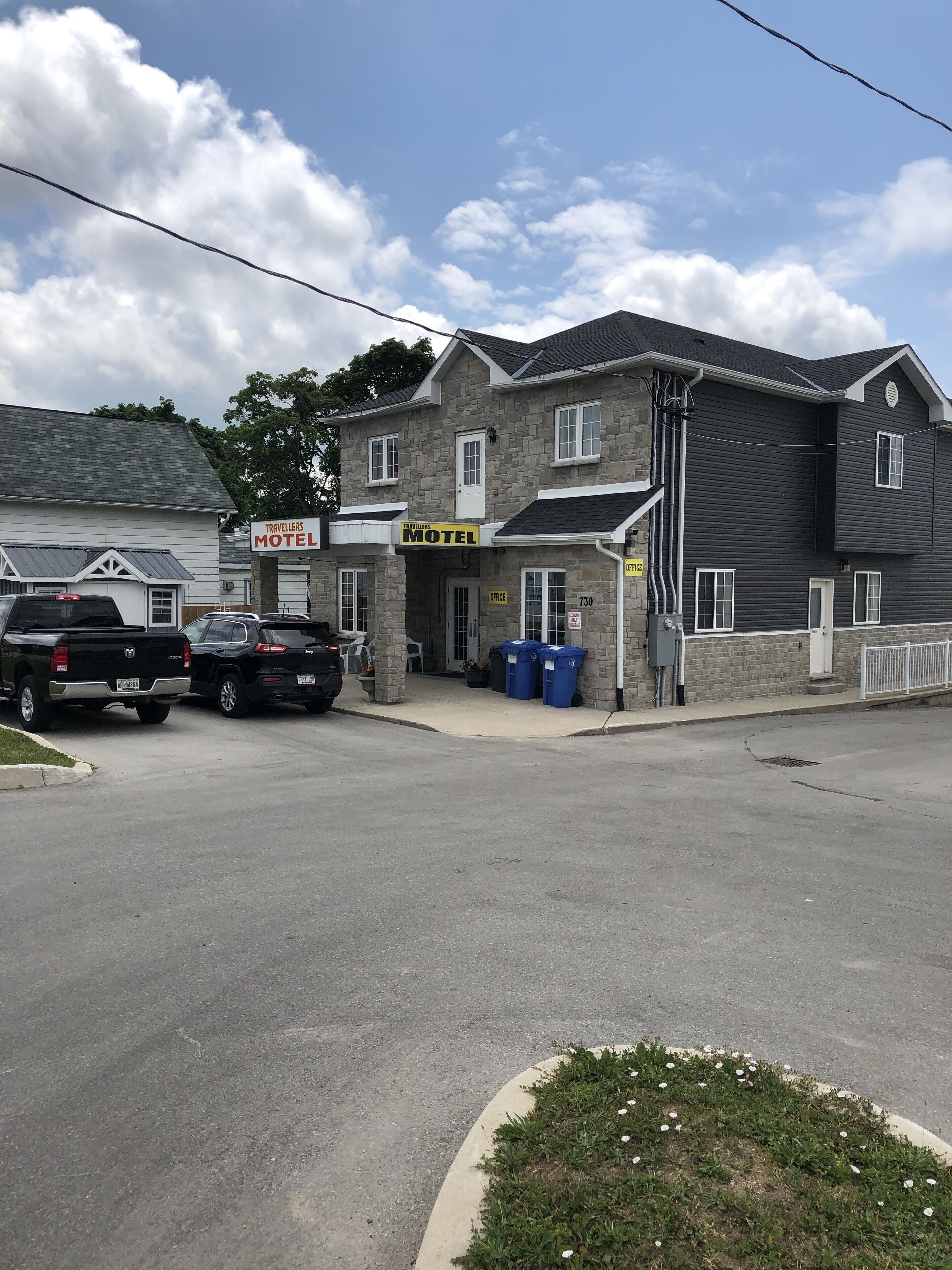 A motel with a stone facade, a signboard, and a parking area with two cars.