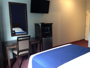 Una habitación de hotel con una cama, un escritorio con una silla, un televisor y un refrigerador.