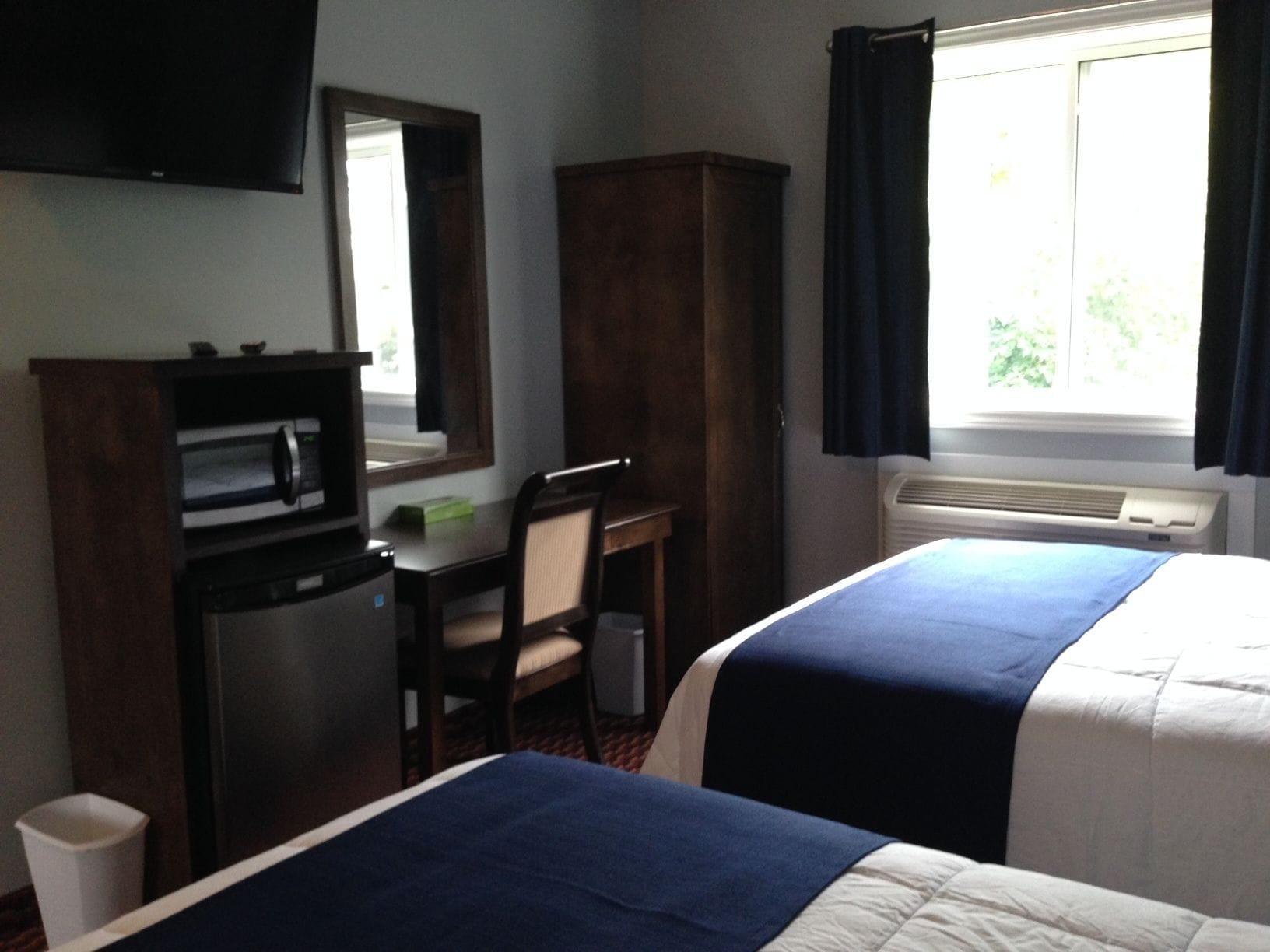 Habitación de hotel con dos camas, un escritorio, una silla, un televisor y una ventana con cortinas.