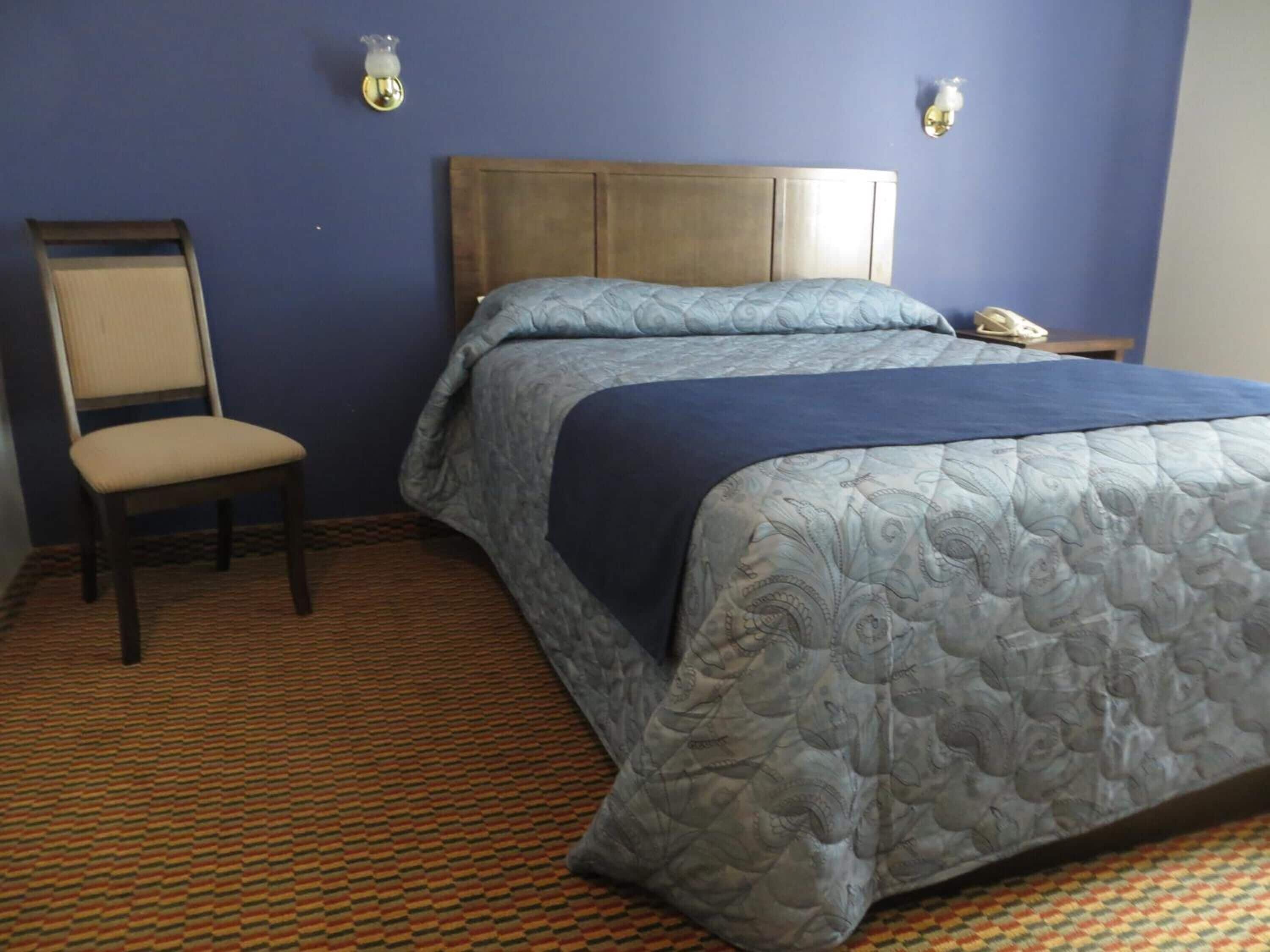 A hotel room with a bed, a chair, and a nightstand with a phone.
