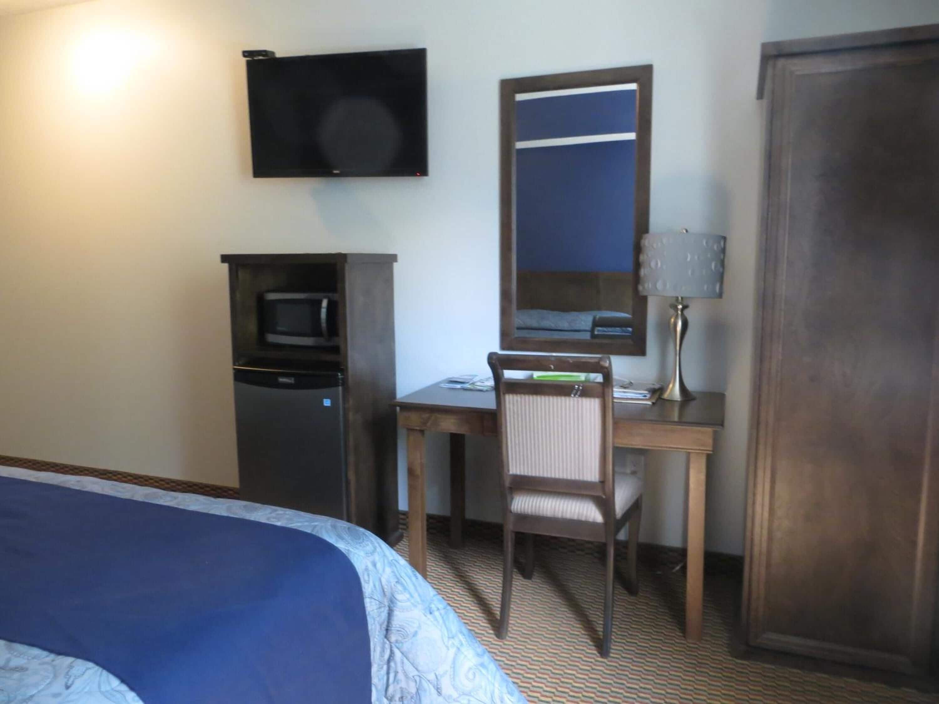 Habitación de hotel con cama, escritorio con silla, televisión, microondas, espejo y armario.