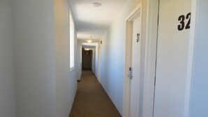 A narrow hallway with carpeted floors and white walls, leading to a door marked with the number 32. - Travellers Motel - New Wing (Owen Sound)