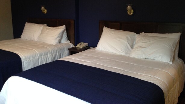 Two single beds with white linens and dark blue bedspreads in a room with dark blue walls and wooden headboards. - Travellers Motel - New Wing (Owen Sound)