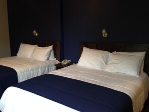 Two single beds with white linens and dark blue bedspreads in a room with dark blue walls and wooden headboards. - Travellers Motel - New Wing (Owen Sound)