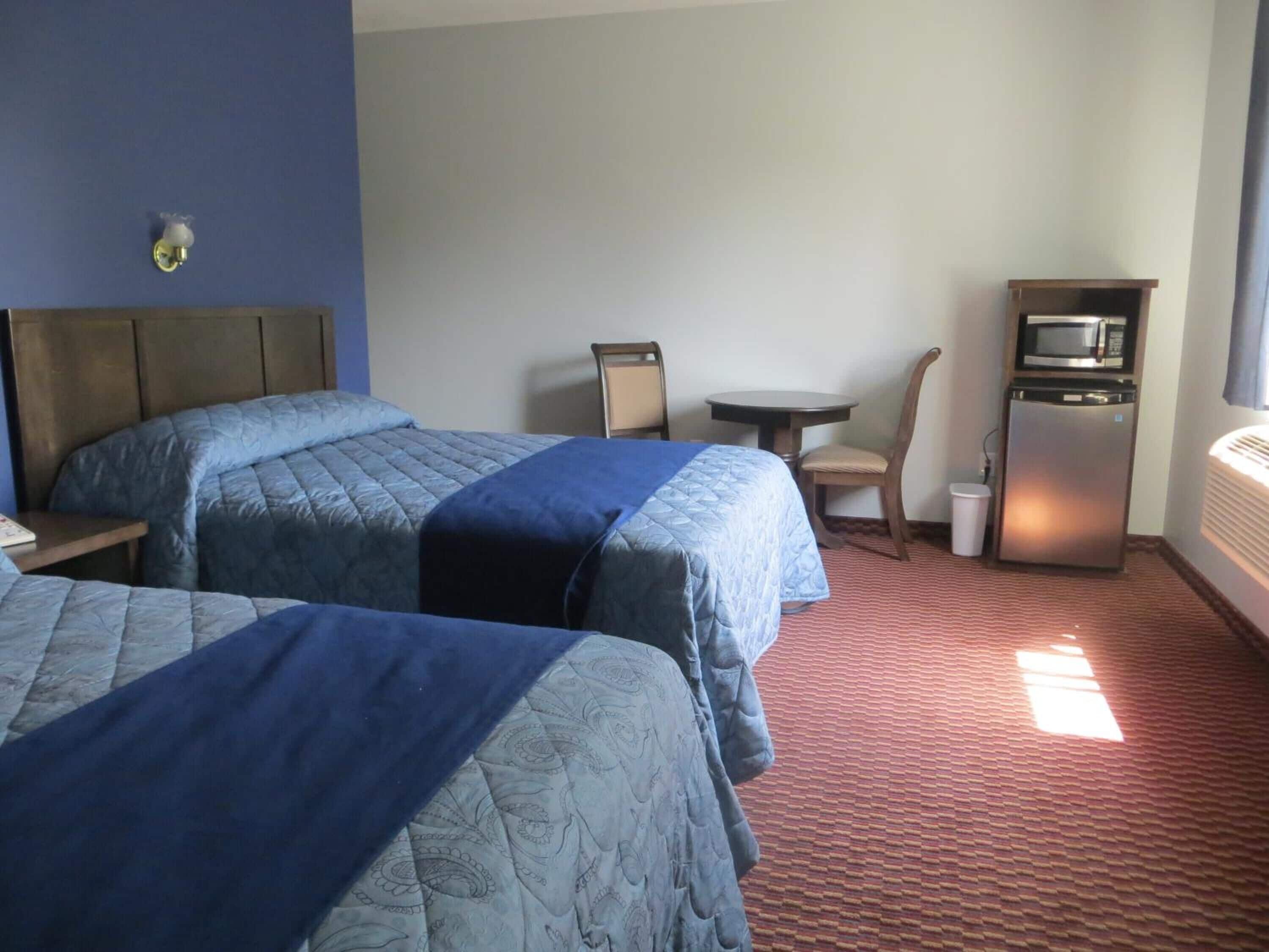 Une chambre d’hôtel avec deux lits, une petite table, une chaise, un four à micro-ondes et un réfrigérateur.