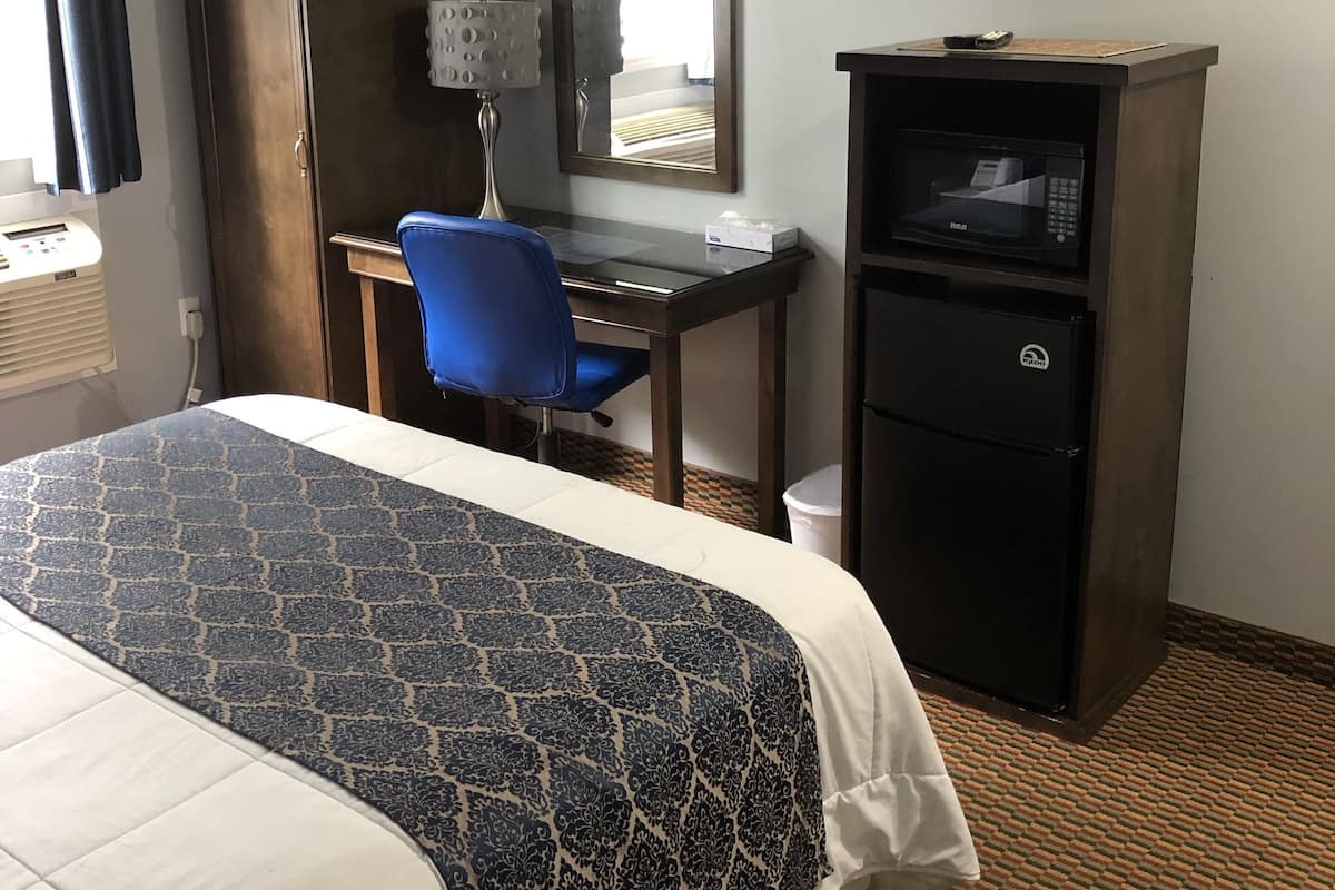 A hotel room with a bed, a desk, a chair, a television, a microwave, and a refrigerator.