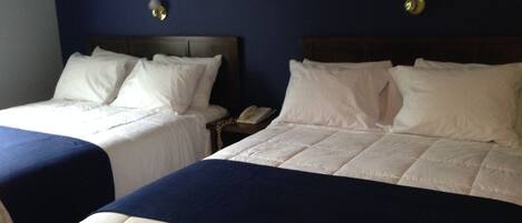 Dos camas individuales con ropa blanca y cabeceros azul oscuro en una habitación de hotel.