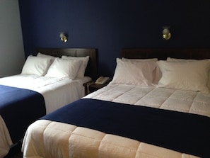 Dos camas individuales con ropa blanca y cabeceros azul oscuro en una habitación de hotel.