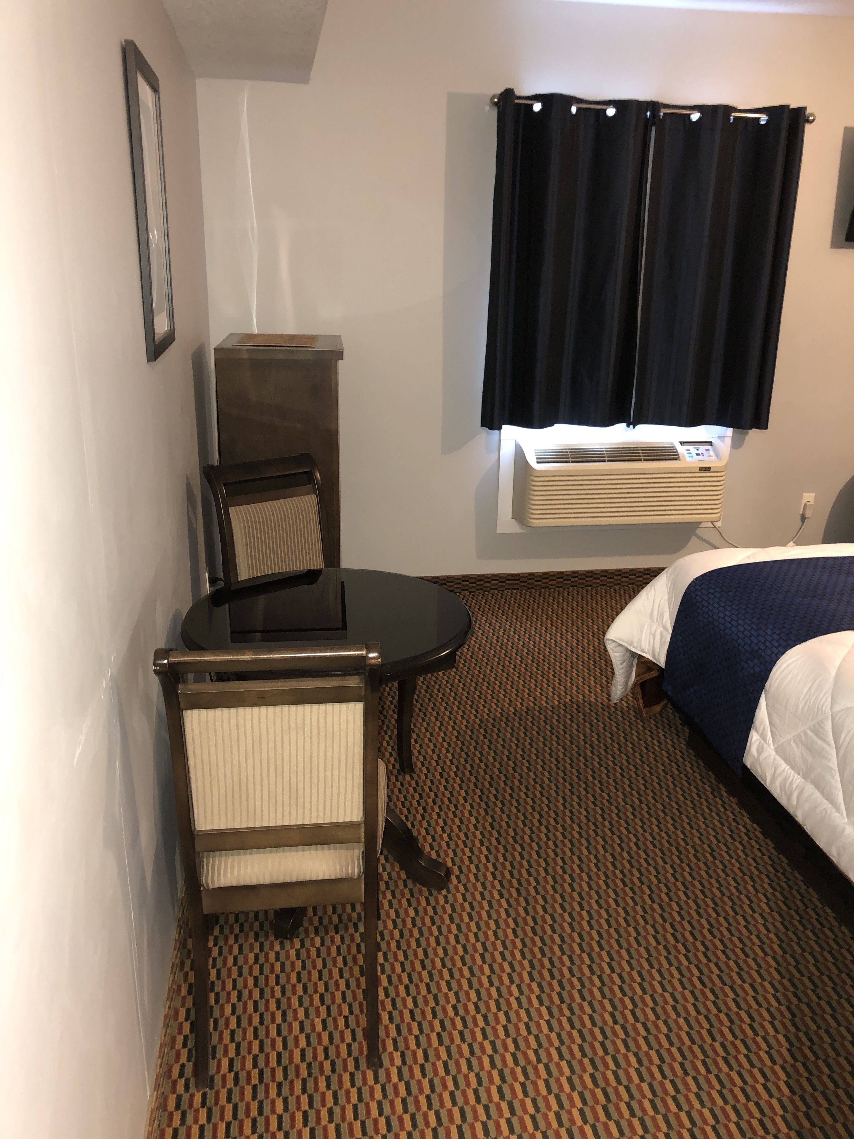 A hotel room with a bed, a desk with a chair, a radiator, and a patterned carpet.
