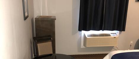 A hotel room with a bed, a desk with a chair, a radiator, and a patterned carpet.
