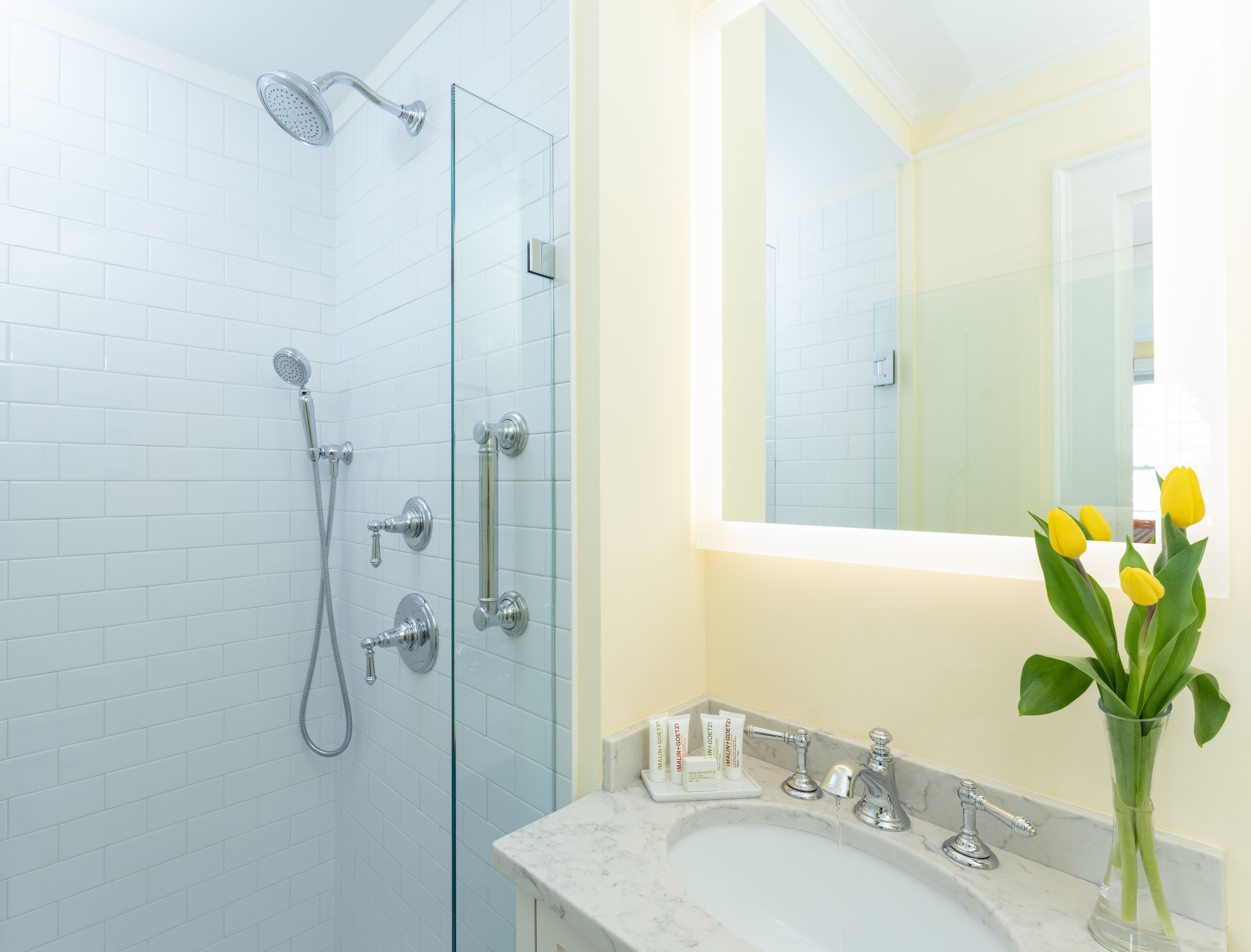 A bathroom with a glass shower enclosure, a sink with a marble countertop, and a mirror above the sink.