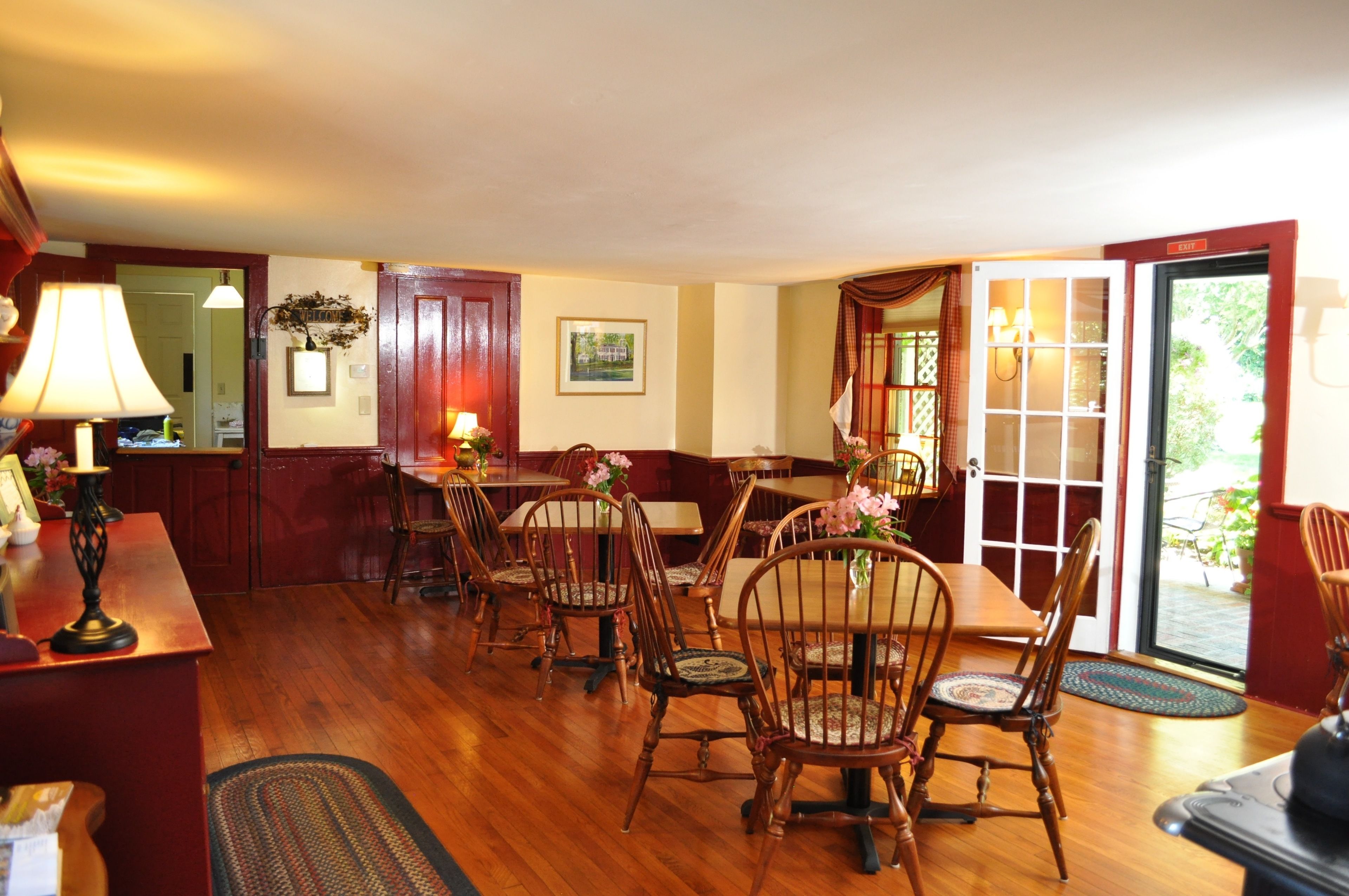 A dining area with wooden chairs and tables, a red door, and a view through a glass door.