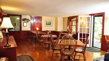 A dining area with wooden chairs and tables, a red door, and a view through a glass door.