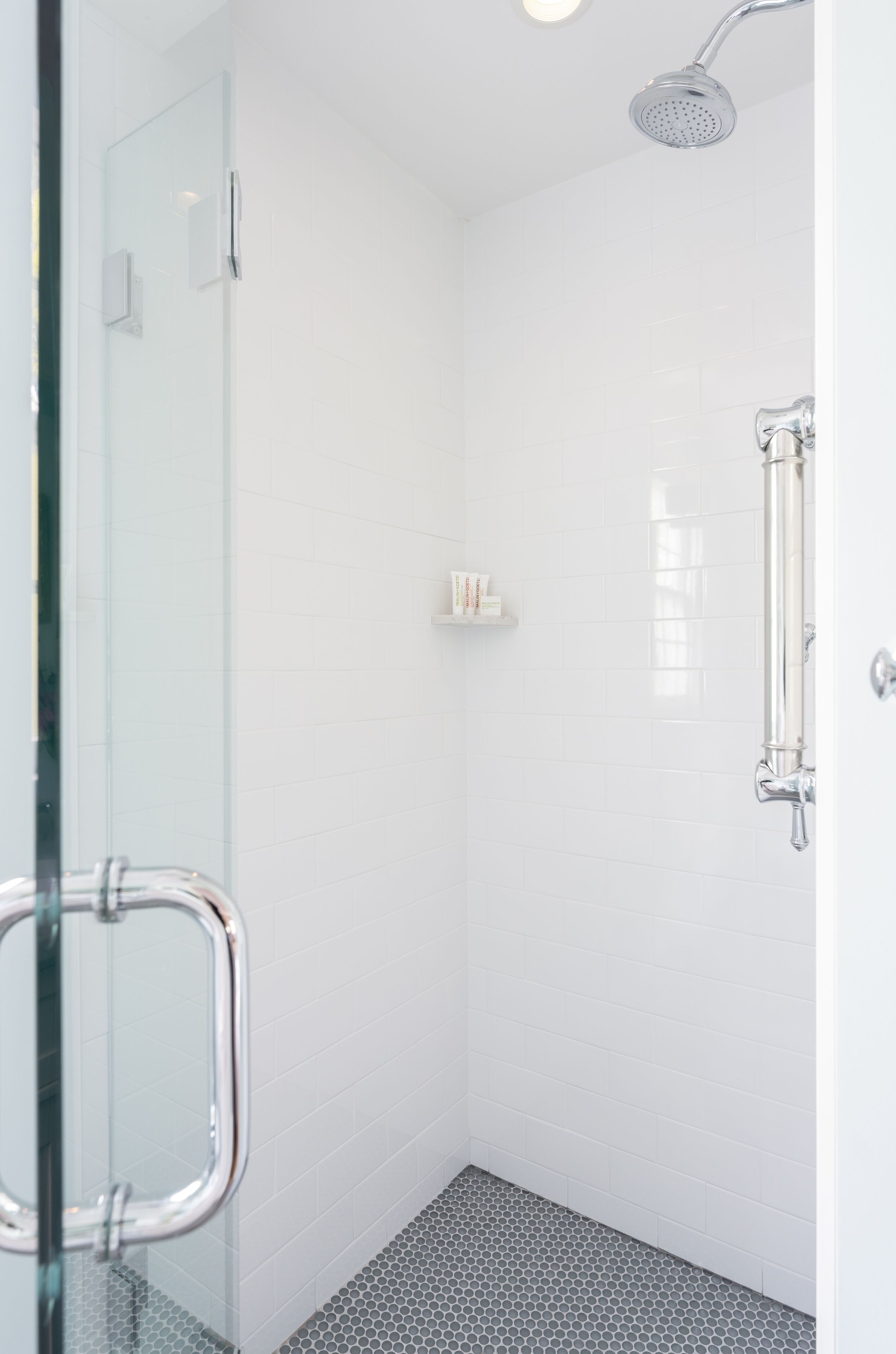 A modern shower with a glass door, white tiled walls, and a hexagonal floor pattern.