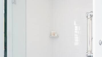A modern shower with a glass door, white tiled walls, and a hexagonal floor pattern.