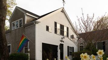 A two-story house with a garage, a flagpole with a rainbow flag, and daffodils in the foreground.