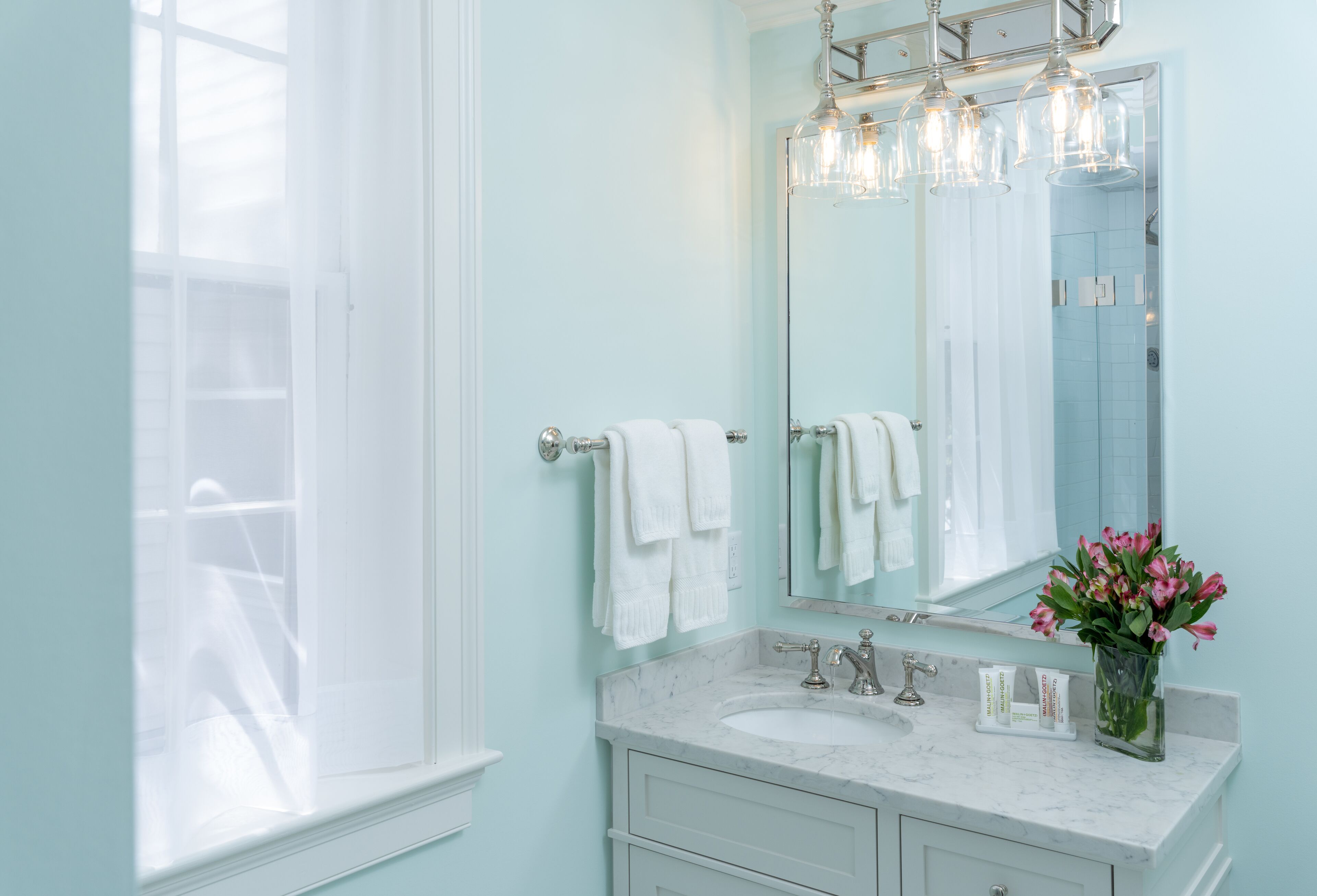 A bathroom with a marble sink, a large mirror, and a window with white curtains.