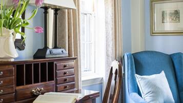 Quarto com escrivaninha de madeira, luminária, cadeira e janela com cortinas.