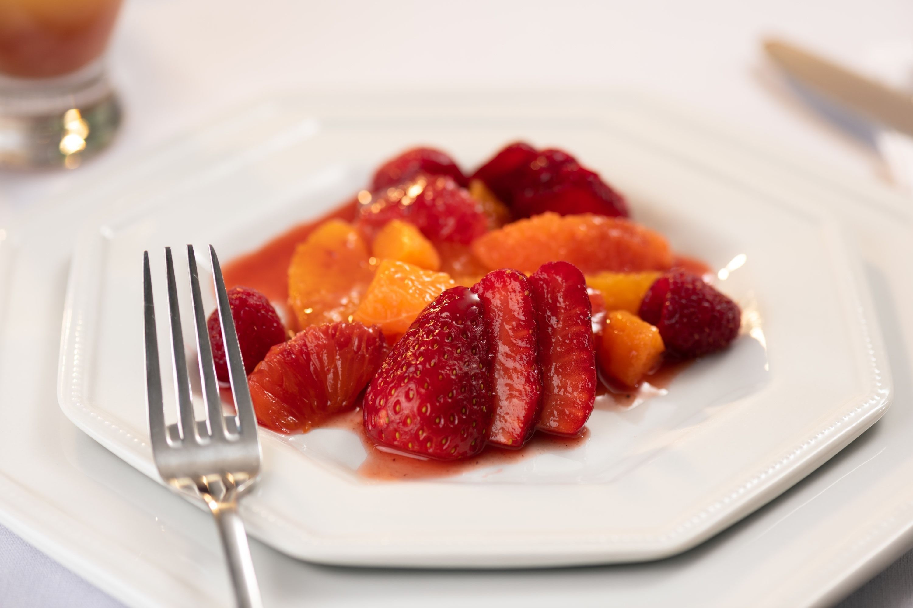 Une assiette blanche garnie de fraises et d’oranges coupées en tranches, accompagnée d’une fourchette.