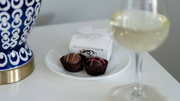 A white table with a blue and gold vase, a glass of white wine, and a box labeled "The Chocolate Sparrow" with chocolates.