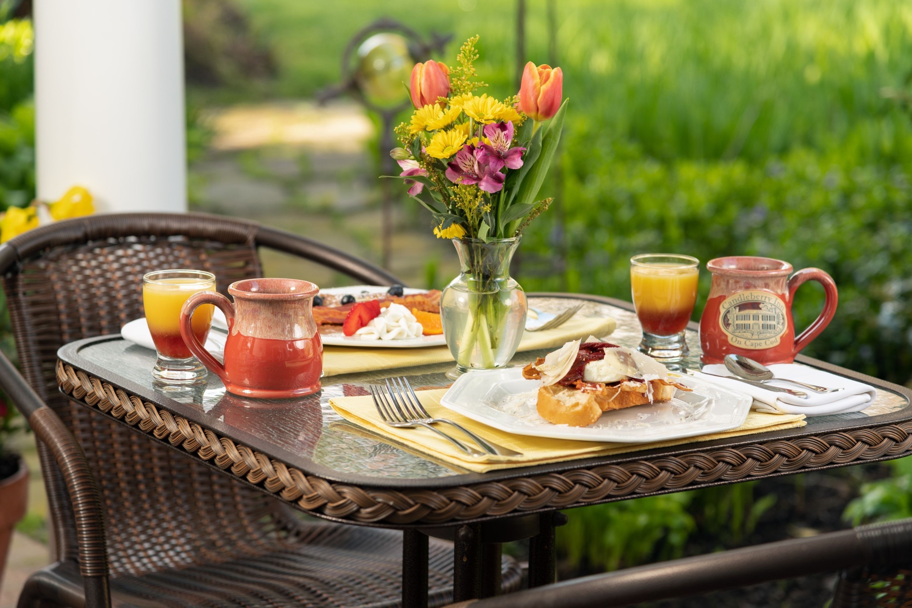 A table set outdoors with a meal, drinks, and a vase of flowers.