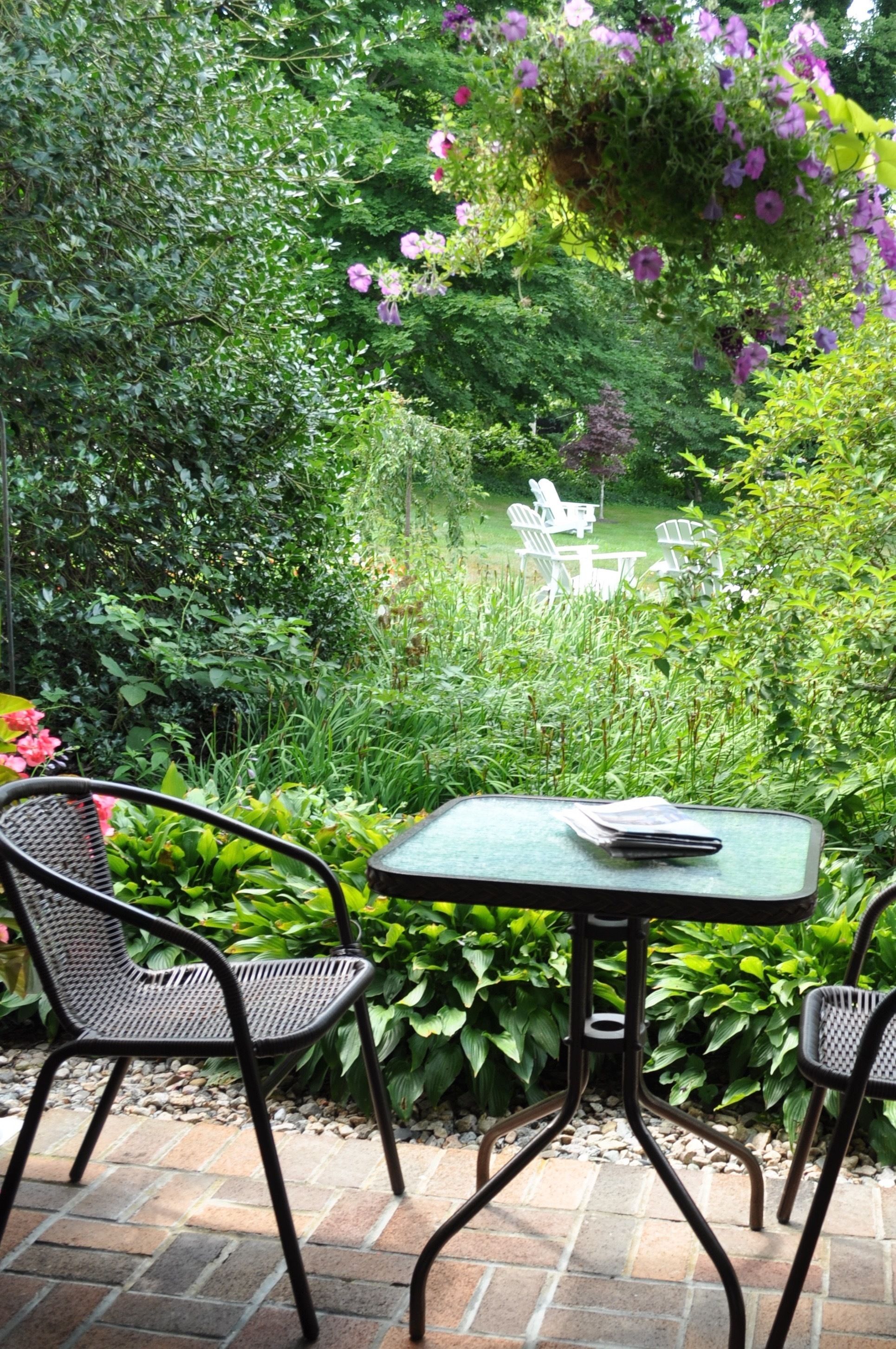 An outdoor patio with a table and chairs, surrounded by lush greenery and flowering plants.