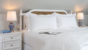 Una cama bien hecha con ropa blanca, dos mesitas de noche con lámparas y un libro sobre la cama.
